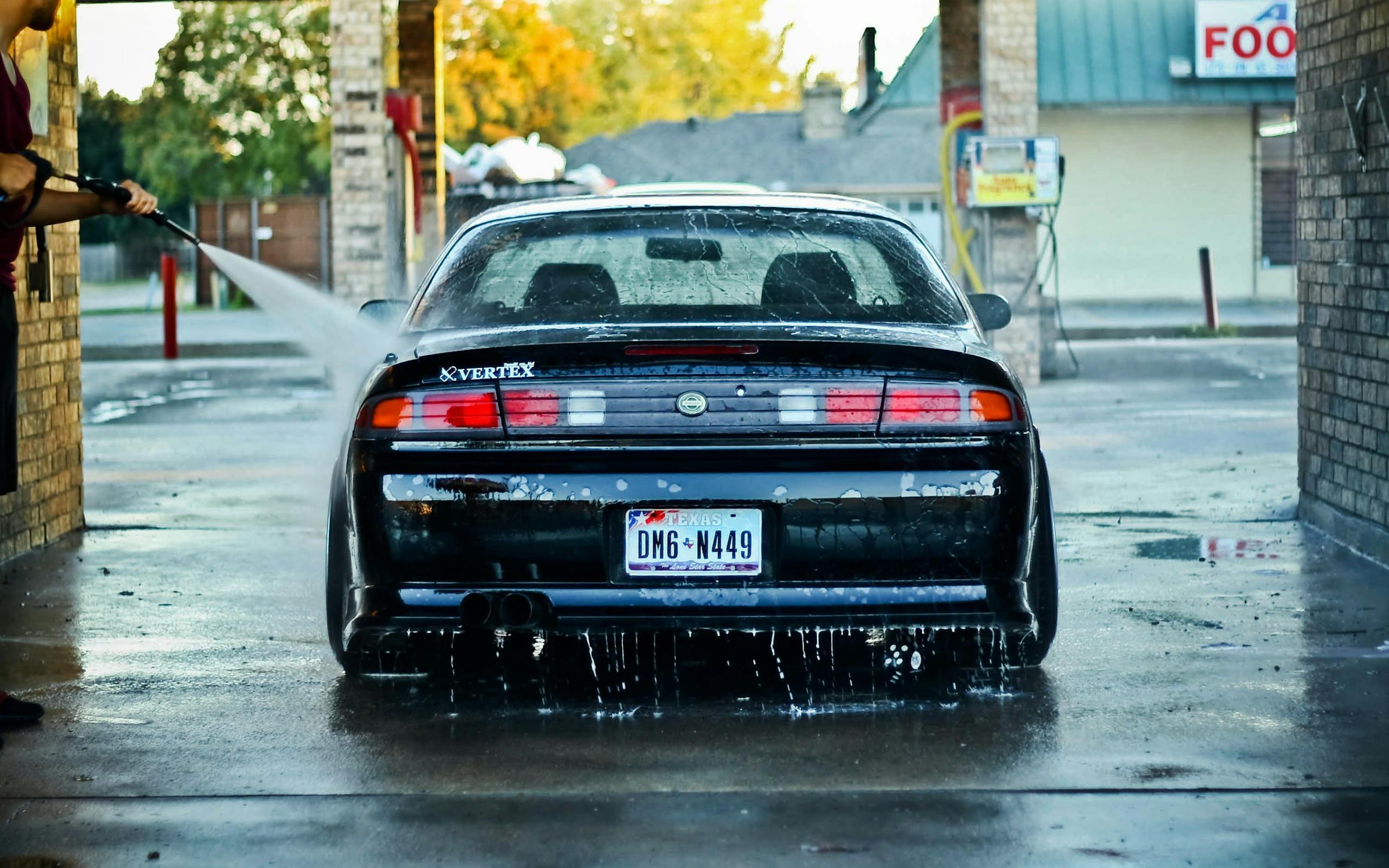 A sleek black car getting washed at an outdoor car wash station on a clear day.