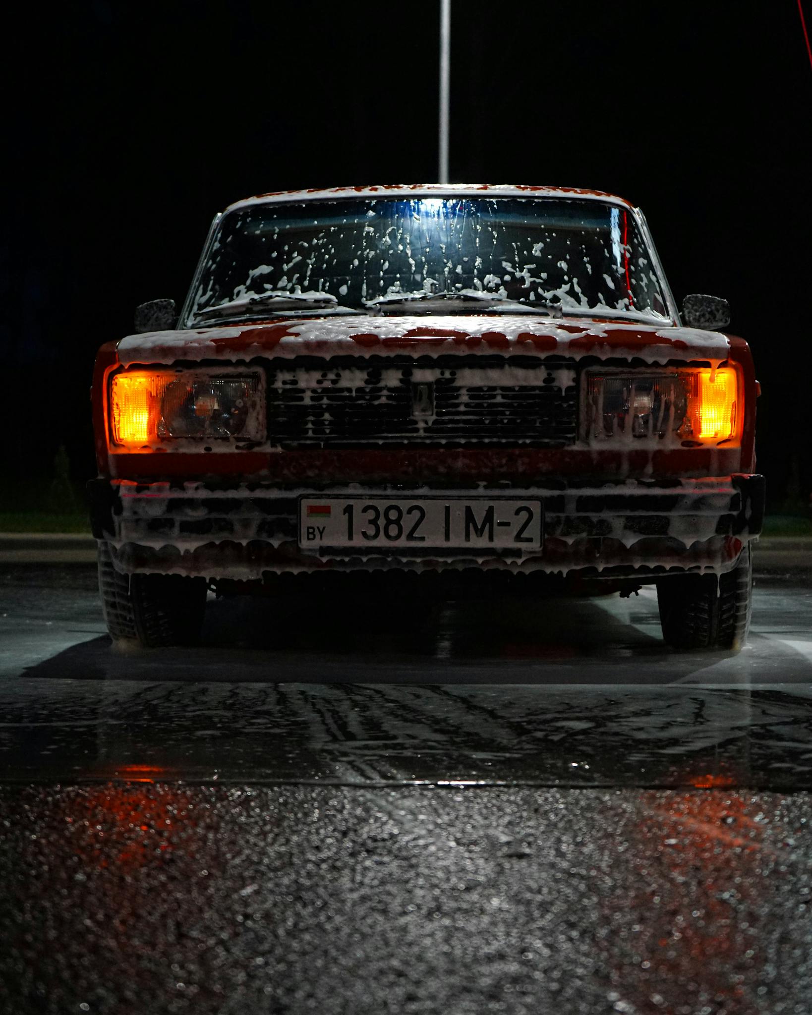 Classic vintage car covered in soap suds during a nighttime car wash session.